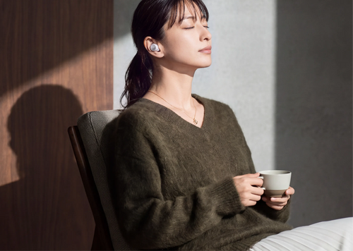日差しの入る部屋でイヤホンを装着してくつろぐ女性